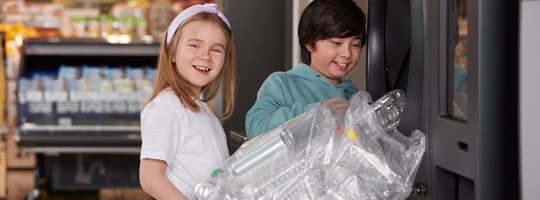 Enfants souriant tenant un sac d'articles vides devant un TOMRA R1