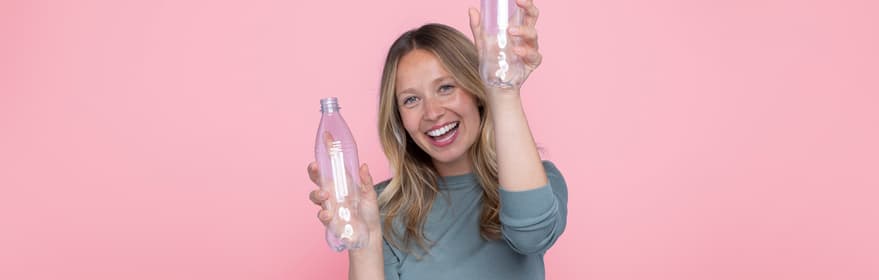 Jente med PET-flasker på rosa bakgrunn