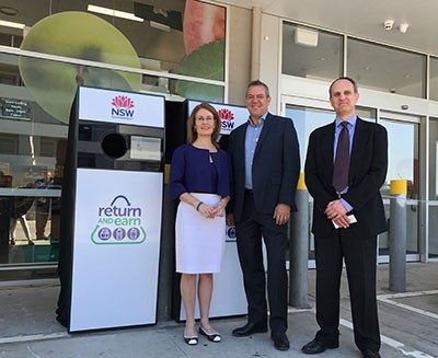 image of a woman and two men standing beside a reverse vending machine