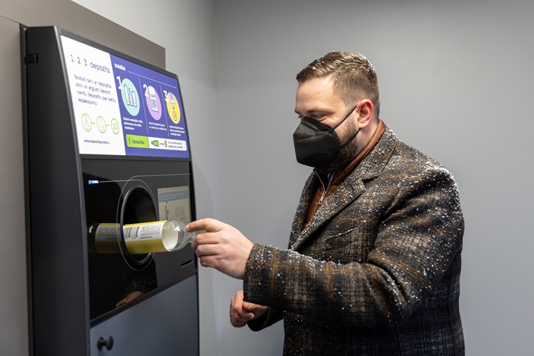 Bild eines Mannes, der eine Flasche in einen Leergutrücknahme-Automaten steckt