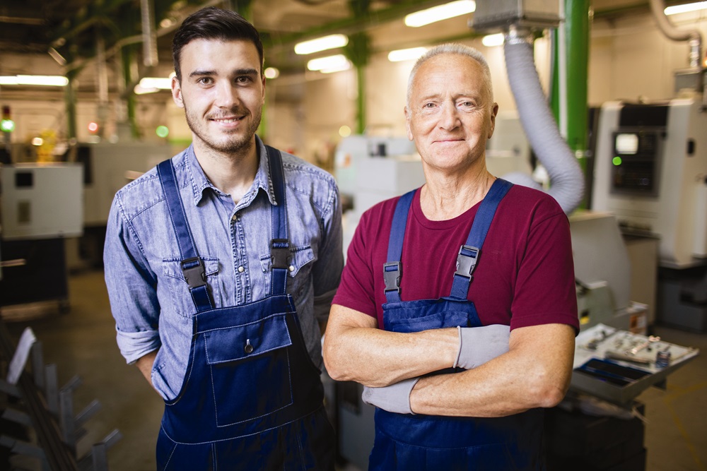 Portrait of two mechanics in overalls standing at his workplace at manufacturing plant with lathe in the background