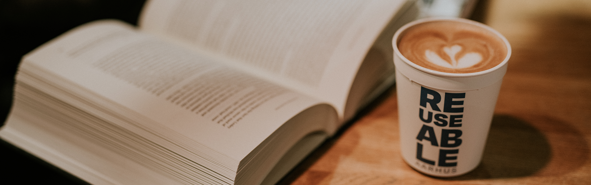 Uma copo de café para viagem REUSEABLE ao lado de um livro aberto