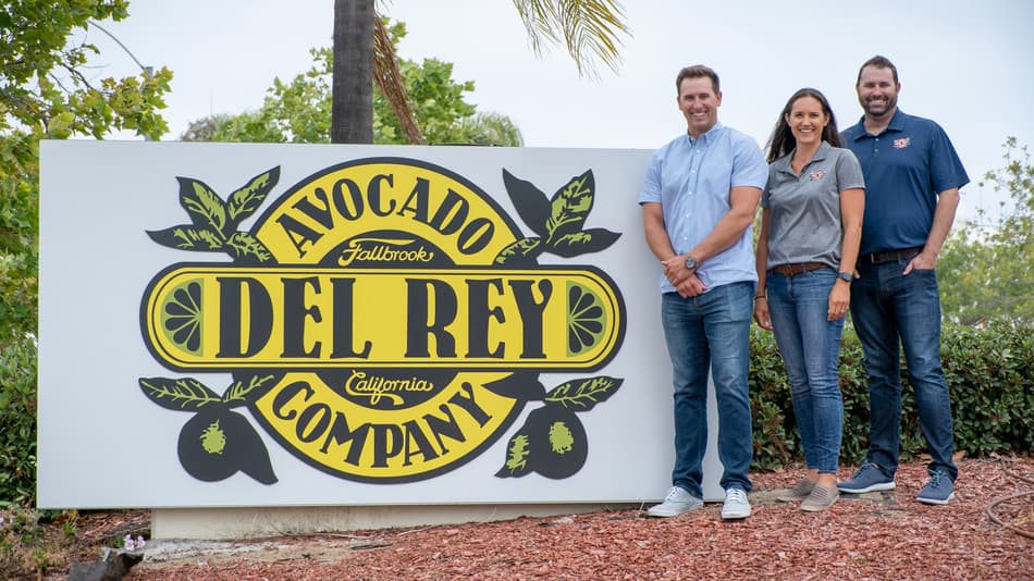 An image of three members of Del ray management in front of their sign