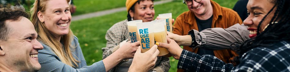 Group of people outdoors holding their REUSEABLE cups together for a cheers
