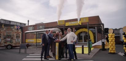 A group of people celebrating outside a supermarket with smoke and balloons.