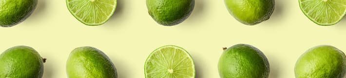 An image of whole limes and limes cut in half and arranged on a light yellow background
