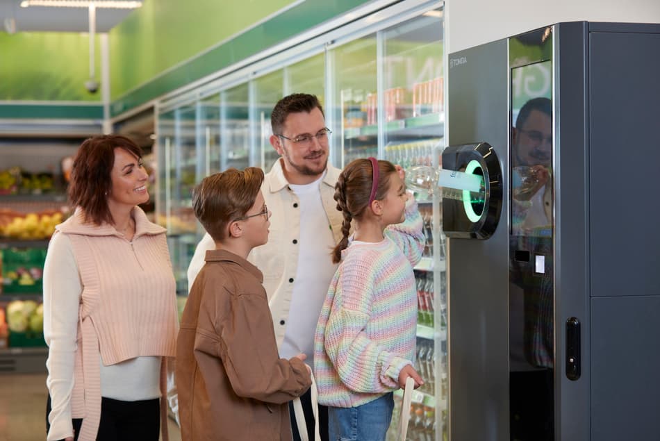 A family recycling a bottle at a TOMRA's reverse vending machine in a grocery store.