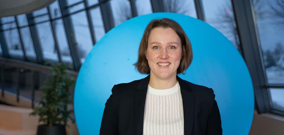 A woman in a suit jacket stands in front of a blue circle