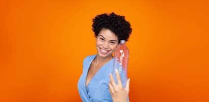 Kvinna mot orange bakgrund som håller en PET-flaska