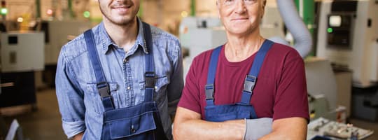 Portrait de deux mécaniciens en vêtements de travail debout sur leur lieu de travail dans une usine de fabrication, avec un tour en arrière-plan