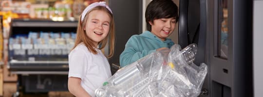 Niños sonriendo sosteniendo una bolsa de envases vacíos delante de una TOMRA R1