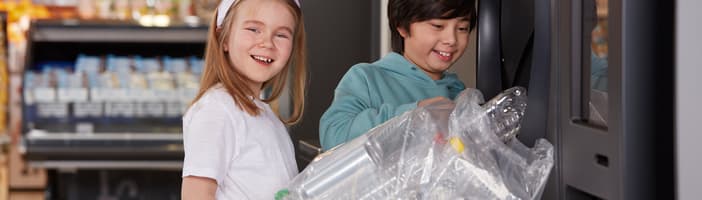 Niños sonriendo sosteniendo una bolsa de envases vacíos delante de una TOMRA R1