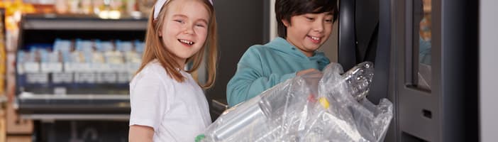 Kids holding a bag of empties  in front of a TOMRA R1 reverse vending machine