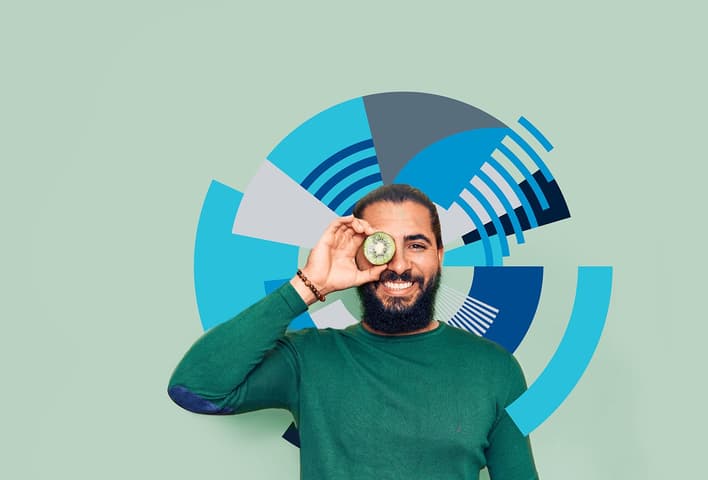 Man with green sweater holding a slice of kiwi fruit up to his eye