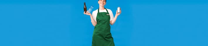 Eine Frau mit grüner Schürze hält gebrauchte Getränkeverpackungen vor blauem Hintergrund