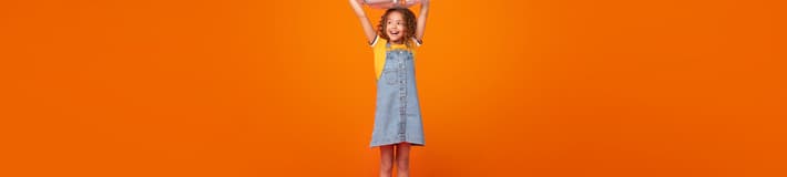 Retrato de una niña con una bolsa llena de botellas sobre un fondo naranja