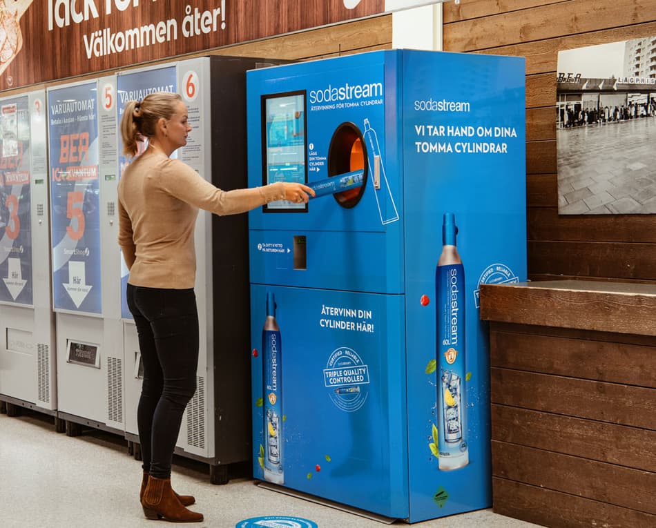 lady feeding sodastream cylinder into a reverse vending machine