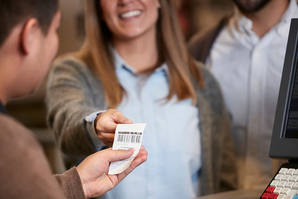 Lächelnde Frau überreicht einen Bon von einem Leergutrücknahme-Automaten