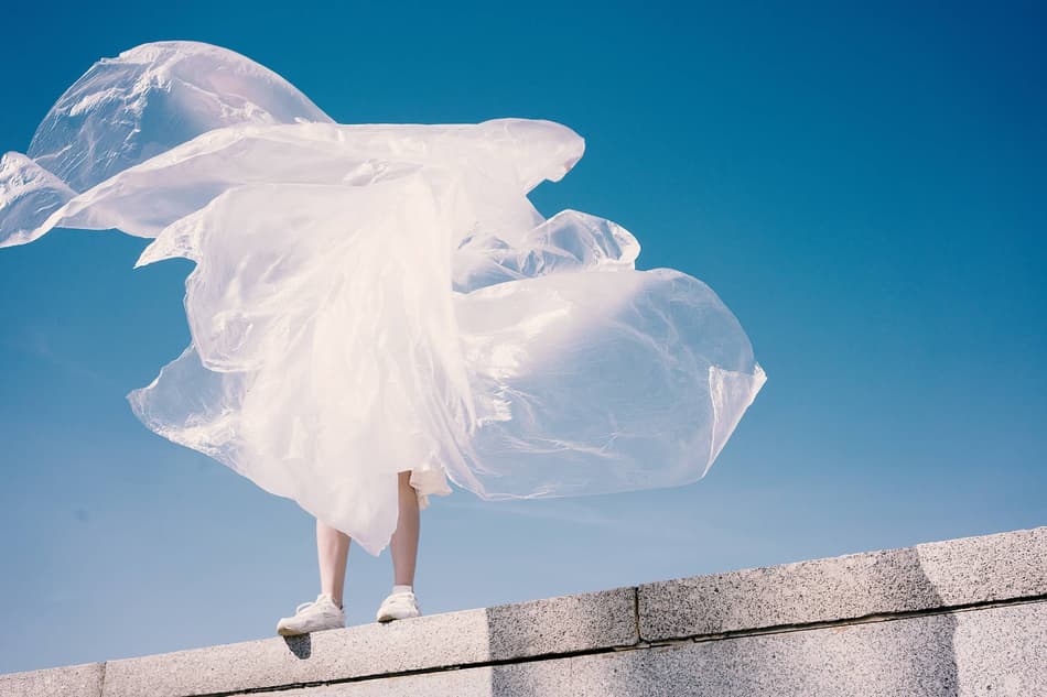 Person wrapped in plastic standing on a ledge with blue sky behind them